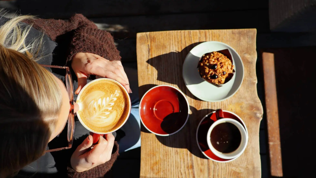 Girl sipping coffee with a muffin on the table in front of her